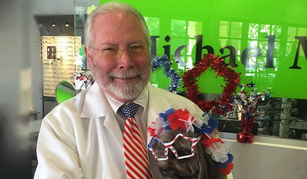 Dr. Michael McQuillan posing with a dog in red, white, and blue attire